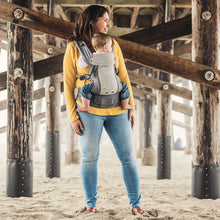 a mother wearing a young boy in a grey cool mesh beco carrier on her front at the beach