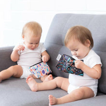 two young children dressed in white onesies sitting on a grey couch with a reusable small snack bag each looking inside