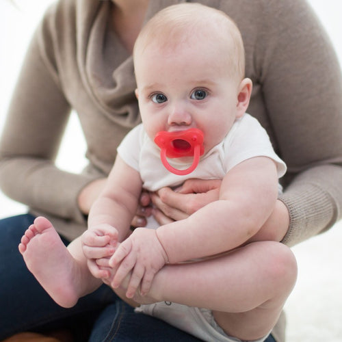 person hold a baby playing with their foot with a one piece silicone pacifier in the mouth