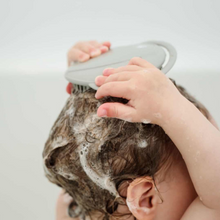 young child using a grey silicone brush to help wash their hair