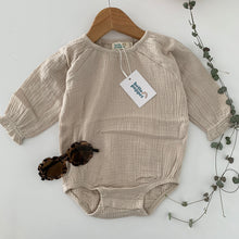 a light beige long sleeve bodysuit with elastic around the legs and domes for nappy changes, small frill around the cuff