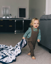 just child walking through a room holding/dragging a white blanket with navy blue edging and planets all over