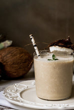 small glass filled with a smoothie on a white plate with a black and white paper straw