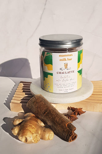 fresh ginger, star anise, cardamom laid together in front of a jar on a white stone circle on a piece of wood