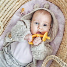 young bay lying in a Moses basinet wearing a knitted cardigan with the hood on holding a teether