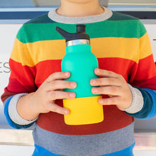 child wearing a bright rainbow striped jumper holding a minty green bottle with a yellow bumper