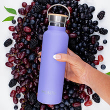 a hand holding a bold bright purple drink bottle in front of blueberries, grapes, blackberries and green leaves