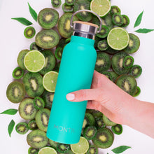a hand holding a bold bright green drink bottle in front of cut up kiwifruit, limes and leaves