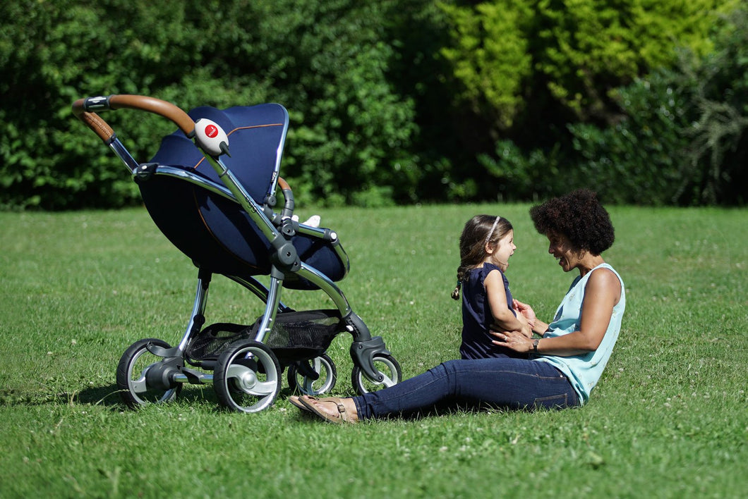 outside on grass, an adult playing with a child, a stroller is beside them with the portable rocker attached 