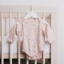 pale peach with white flowers all over it on a hanger on a wooden cot with white sheets