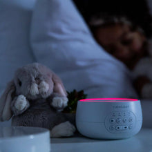 dark bedroom with person asleep, a soft bunny toy sitting beside the white noise machine with the red night light glowing