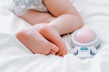 daylight photo of a young child sleeping on white sheets with the soother positioned near their feet at the bottom of the sleep area